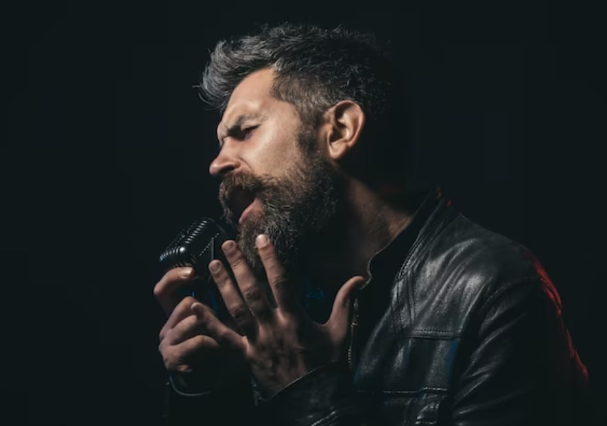 a bearded man in a black leather jacket holding a microphone and singing