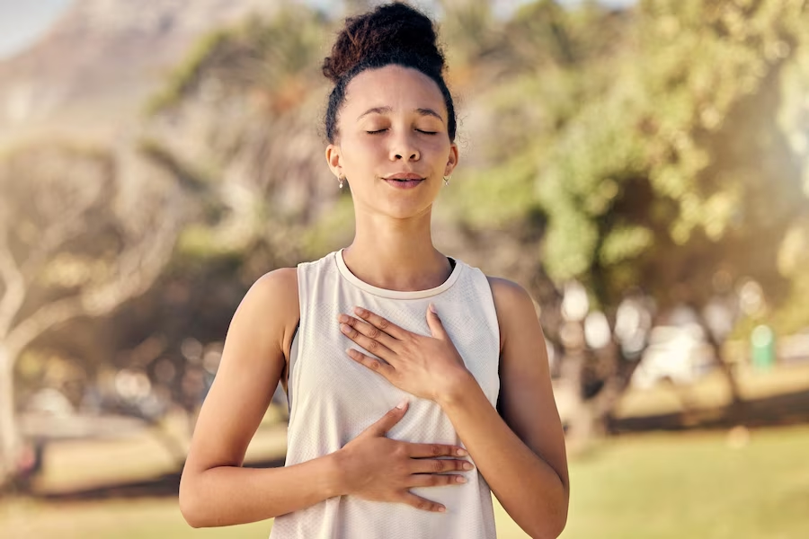 Image of a woman outdoors, holding her chest and diaphragm with her eyes closed