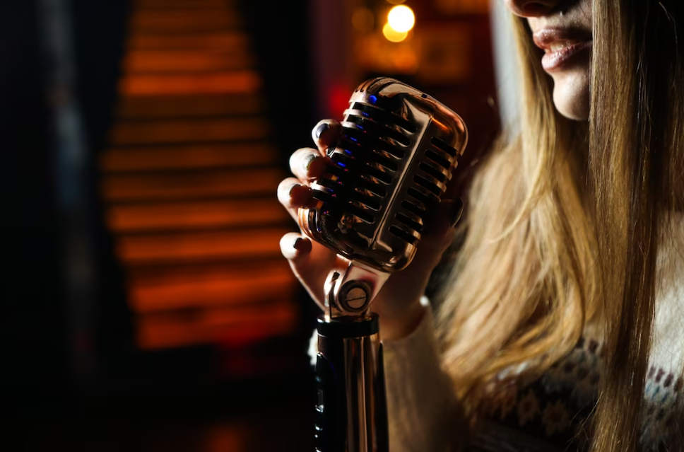 woman with long hair in a sweater holds a microphone in the red room