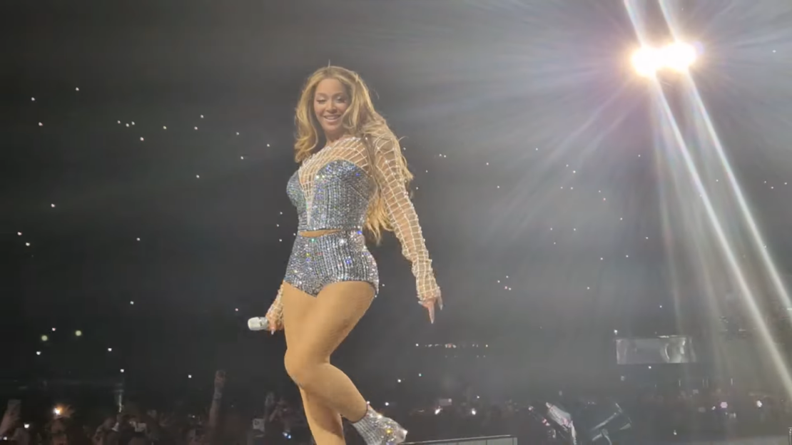 Beyonce in a shiny dress, dancers in black costumes, and people with instruments on the stage