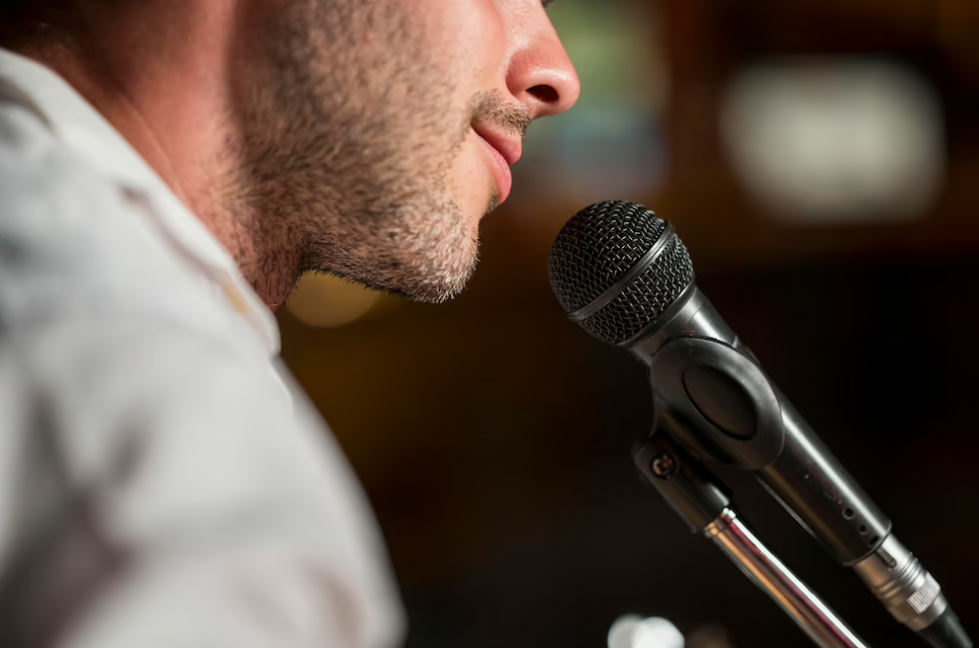 smiling man singing at the microphone, blurred background behind him